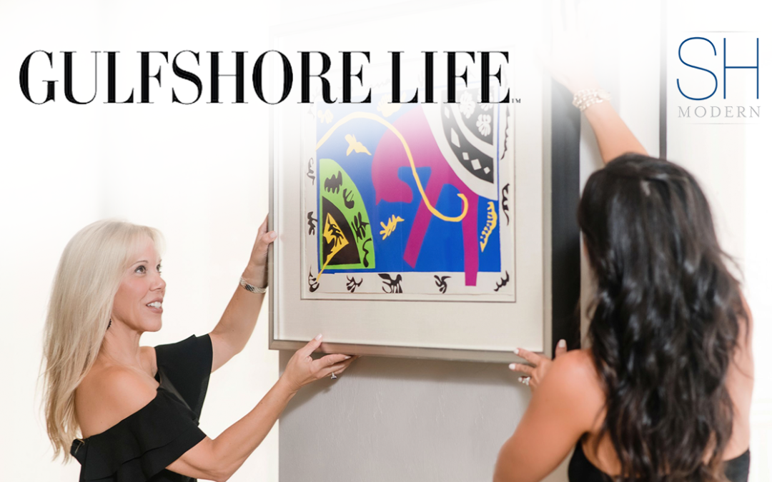 Two women hanging colorful abstract art in a stylish room.